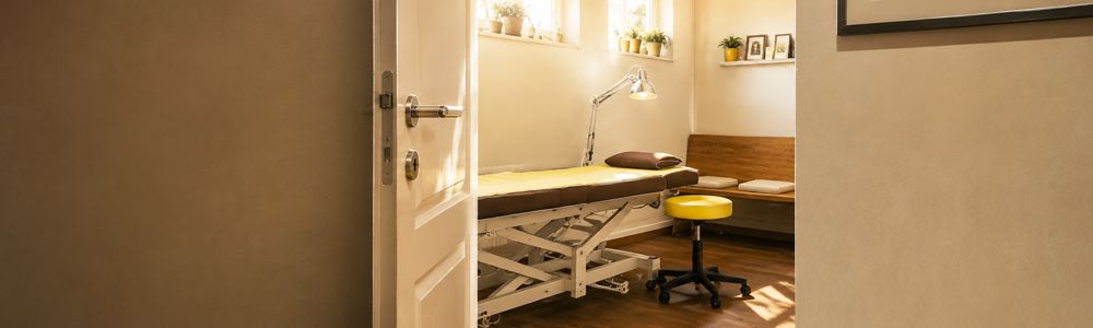 Geöffnete Praxistür mit Blick auf Behandlungsliege im Therapiezentrum Westfalen